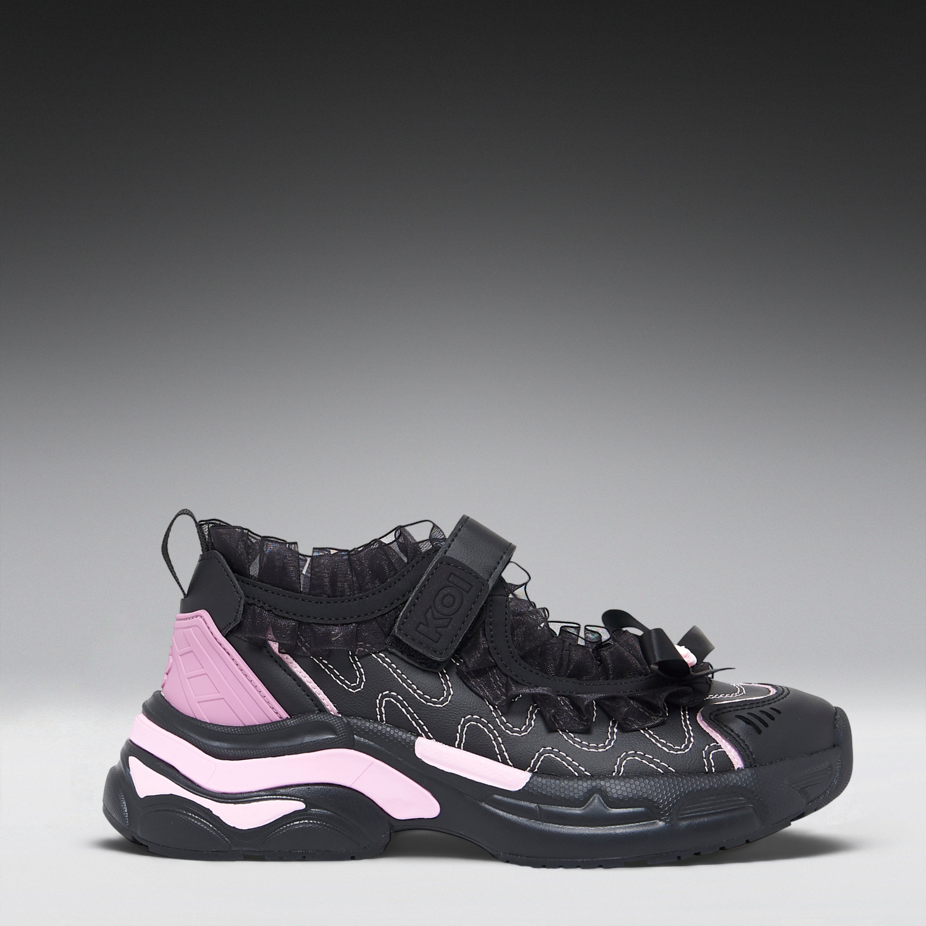A black high-top sneaker with light pink accents on the heel and midsole, featuring a strap closure and textured synthetic overlays, shown against a dark gray gradient background.