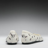 A pair of off-white ballet flats with a black ant print pattern, shown from the back against a dark-to-light gray gradient background.