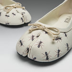 A pair of split-toe ballet flats with an off-white base, printed with black and brown ants, and finished with a beige rope bow on the top, shown on a gray gradient background.
