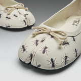 A pair of split-toe ballet flats with an off-white base, printed with black and brown ants, and finished with a beige rope bow on the top, shown on a gray gradient background.