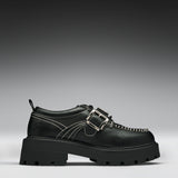 A black leather platform shoe with double buckle straps, contrast white stitching, and a chunky lug sole, shown in a side profile on a gray gradient background.
