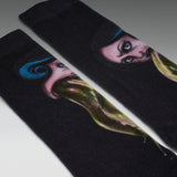 A pair of black crew socks featuring a detailed graphic print of a woman's face with blue hair and a long green mustache, photographed on a neutral gray background.
