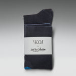 A pair of dark charcoal gray crew socks folded together with a white paper label that reads 'KOI x Junji Ito Collection'. A small light blue accent is visible on the toe area.