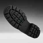 A close-up of a black rubber shoe sole with deep lugs and a textured tread pattern, shown against a dark-to-light gray gradient background.