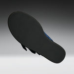 The black outsole of a flat sandal, shown floating against a dark gray to light gray gradient background. A small portion of the blue upper is visible on the right side.