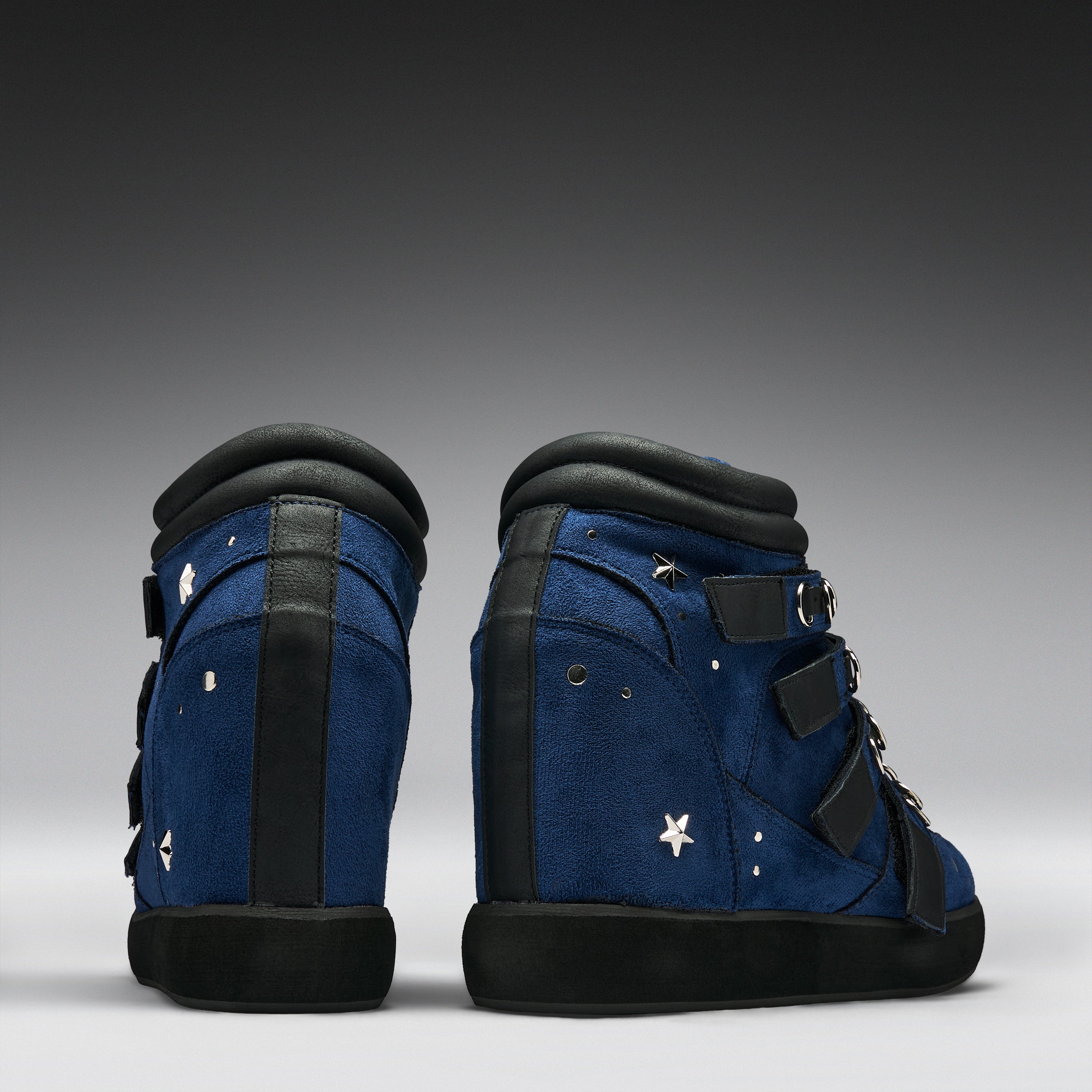 A pair of high-top blue sneakers with black soles, black straps, and white star details, shown from the back and side against a dark gray gradient background.