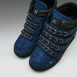 A pair of high-top blue suede boots with black leather trim, multiple rows of silver metal eyelets, and a black sole, shown on a neutral gray background.