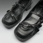 A pair of black Mary Jane-style shoes with textured spiral embellishments on the straps, shown on a neutral gray background. The brand name 'IOKZO' is visible on the insole.