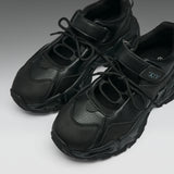 A pair of chunky black sneakers with a textured leather and mesh upper, featuring thick sculpted soles and hook-and-loop strap closures, shown on a neutral gray background.