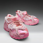 A pair of chunky pink sneakers with shiny metallic pink panels, fuzzy faux-fur trim, and pink laces, photographed on a clean gray studio background.