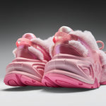 A pair of chunky pink winter sneakers with fluffy white faux-fur trim and glossy metallic pink uppers, shown from a low angle against a dark-to-light gray gradient background.
