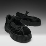 A pair of black Mary Jane platform shoes with textured soles, black mesh side panels, and silver studs, displayed on a gray gradient studio background.