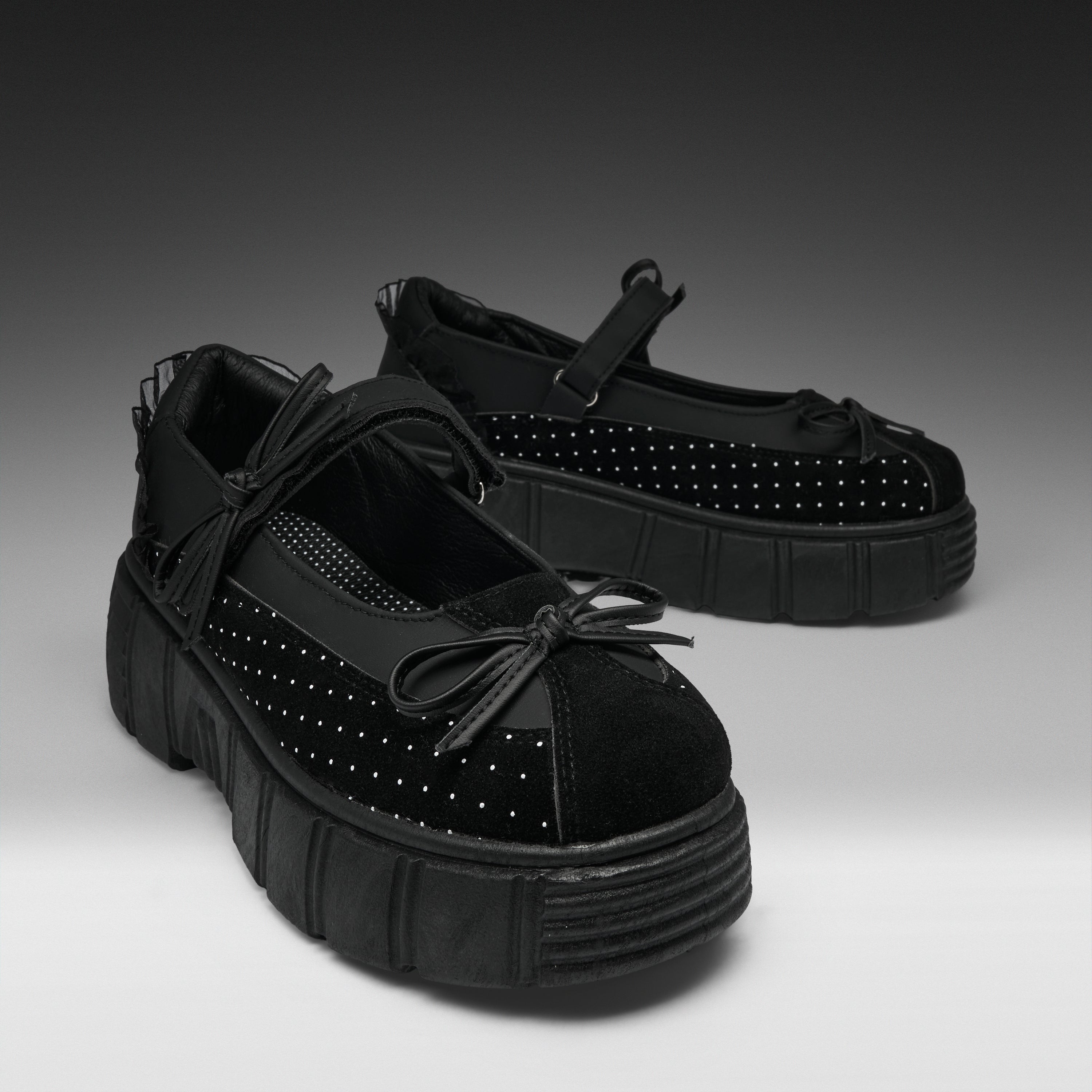 A pair of black Mary Jane platform shoes with textured soles, black mesh side panels, and silver studs, displayed on a gray gradient studio background.