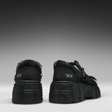 A pair of black platform sneakers shown from the back, featuring chunky lug soles, black laces, and the brand name 'KOI' printed in white on the heel.