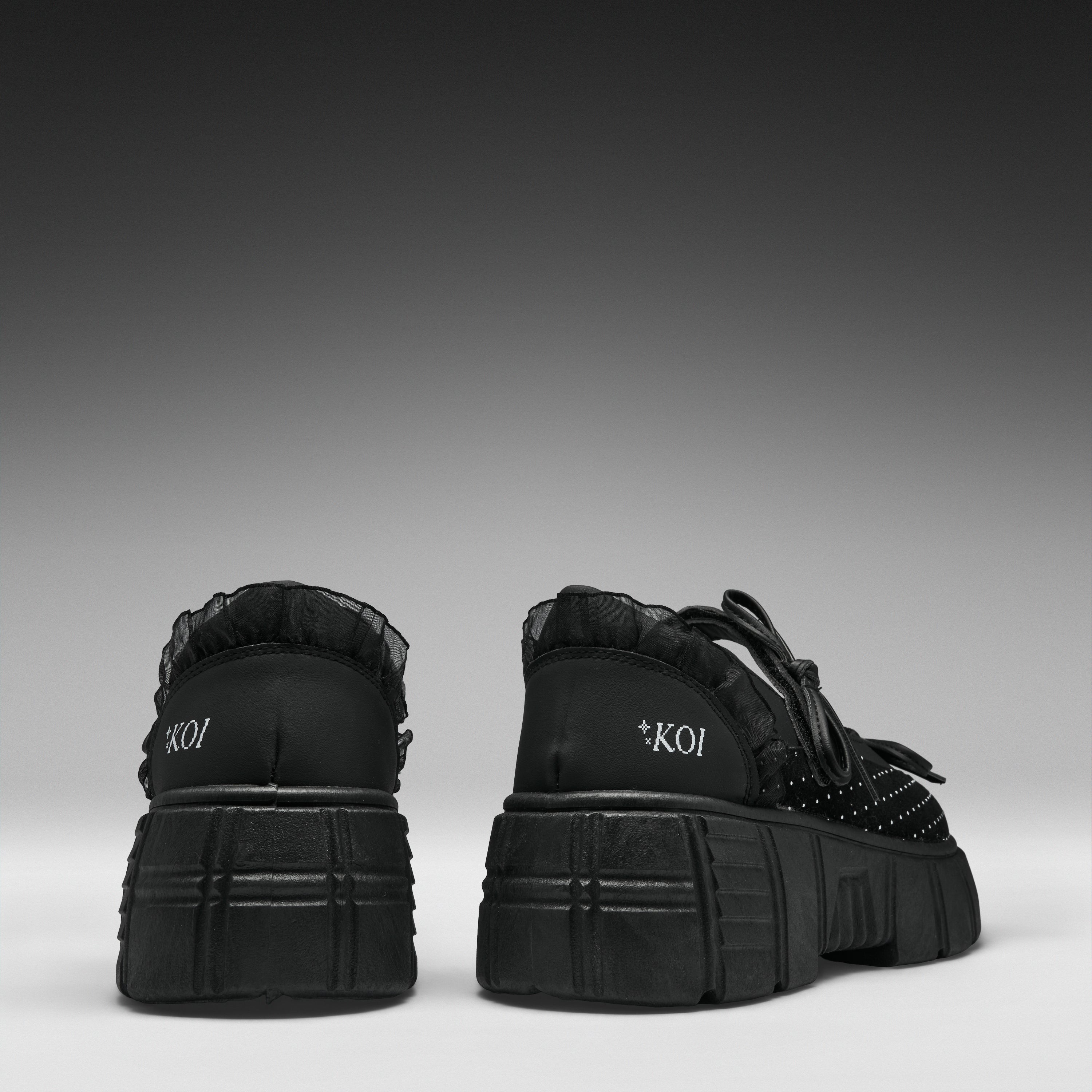 A pair of black platform sneakers shown from the back, featuring chunky lug soles, black laces, and the brand name 'KOI' printed in white on the heel.