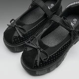 A pair of black platform Mary Jane shoes with suede toe caps, perforated details, and bow accents, shown on a neutral gray background.