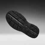A black rubber shoe sole shown from a top-down angle against a dark gray to light gray gradient background.
