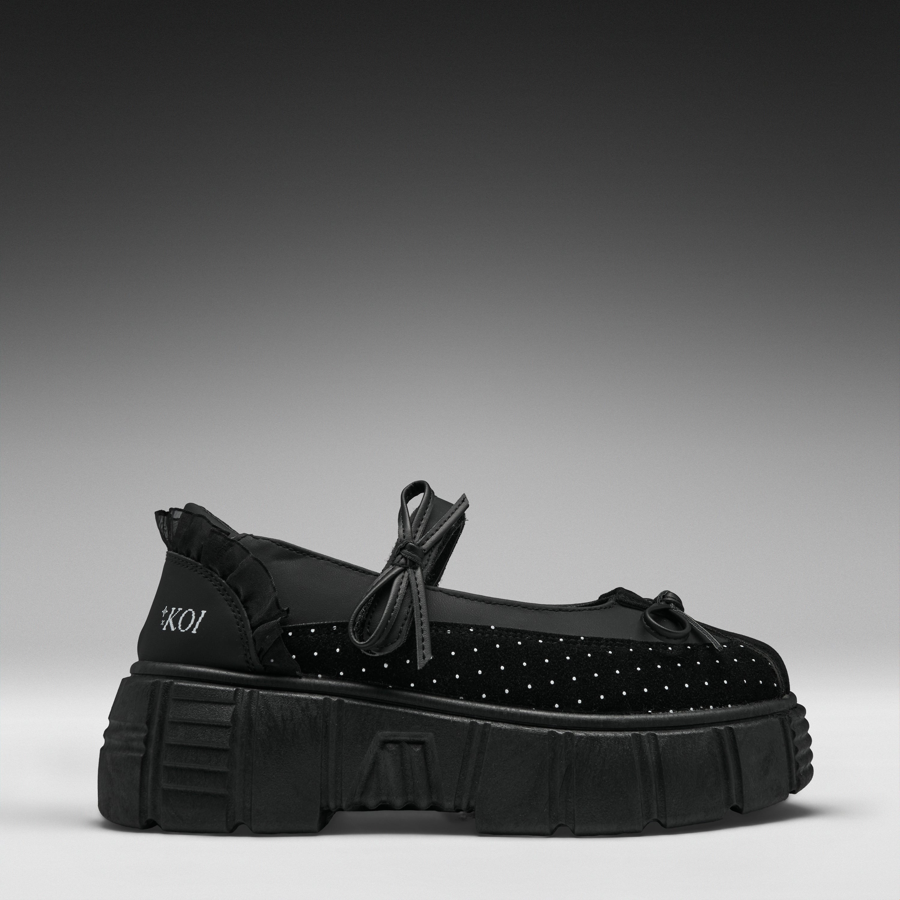 A single black platform Mary Jane shoe with a textured sole, black polka-dot toe box, and a small white brand logo on the heel, set against a dark gray gradient background.