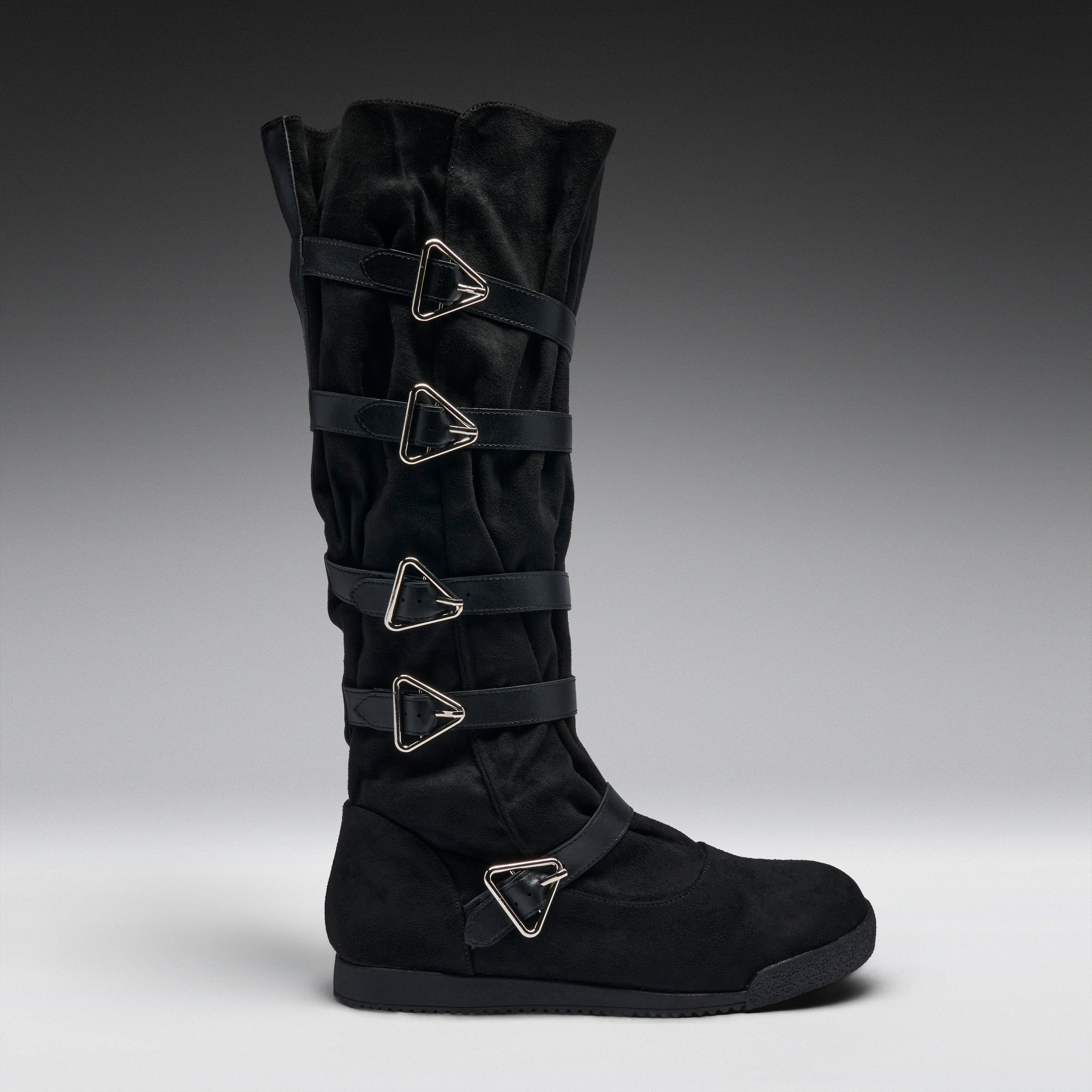A black suede knee-high boot featuring four wrap-around straps with silver-tone triangular metal buckles, shown in profile against a dark gray gradient background.