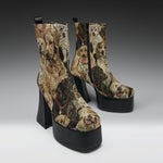 A pair of platform ankle boots with high block heels, featuring a woven dog pattern in earthy tones on a light gray studio background.