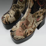 A pair of high-heeled platform ankle boots featuring a detailed woven tapestry pattern of various dog faces in earthy tones of brown, beige, and black, with solid black platform soles.
