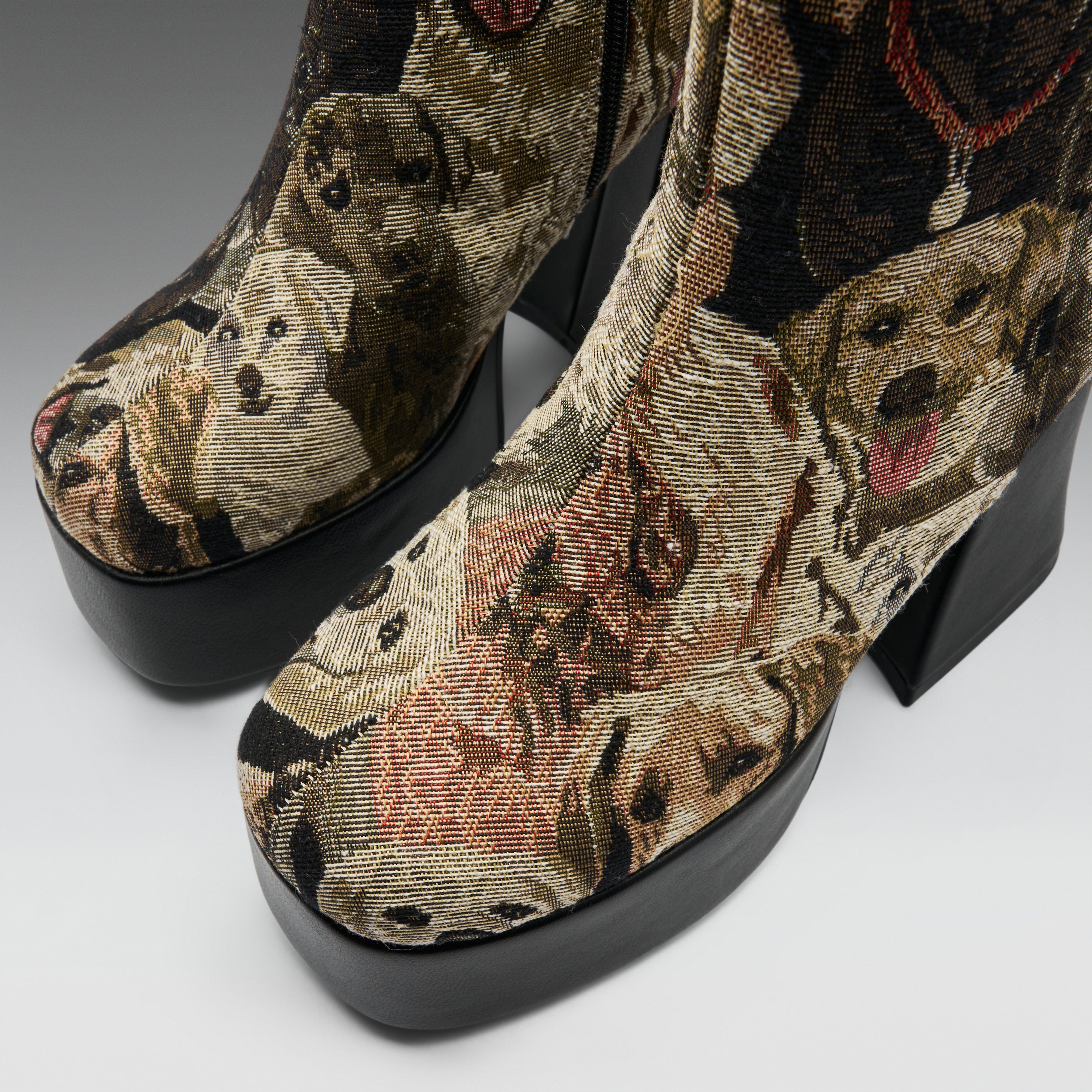 A pair of high-heeled platform ankle boots featuring a detailed woven tapestry pattern of various dog faces in earthy tones of brown, beige, and black, with solid black platform soles.