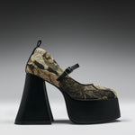 A single high-heeled platform Mary Jane shoe with a black platform and heel, and a pointed toe covered in a green, brown, and black floral brocade fabric. It features a black ankle strap with a silver buckle.