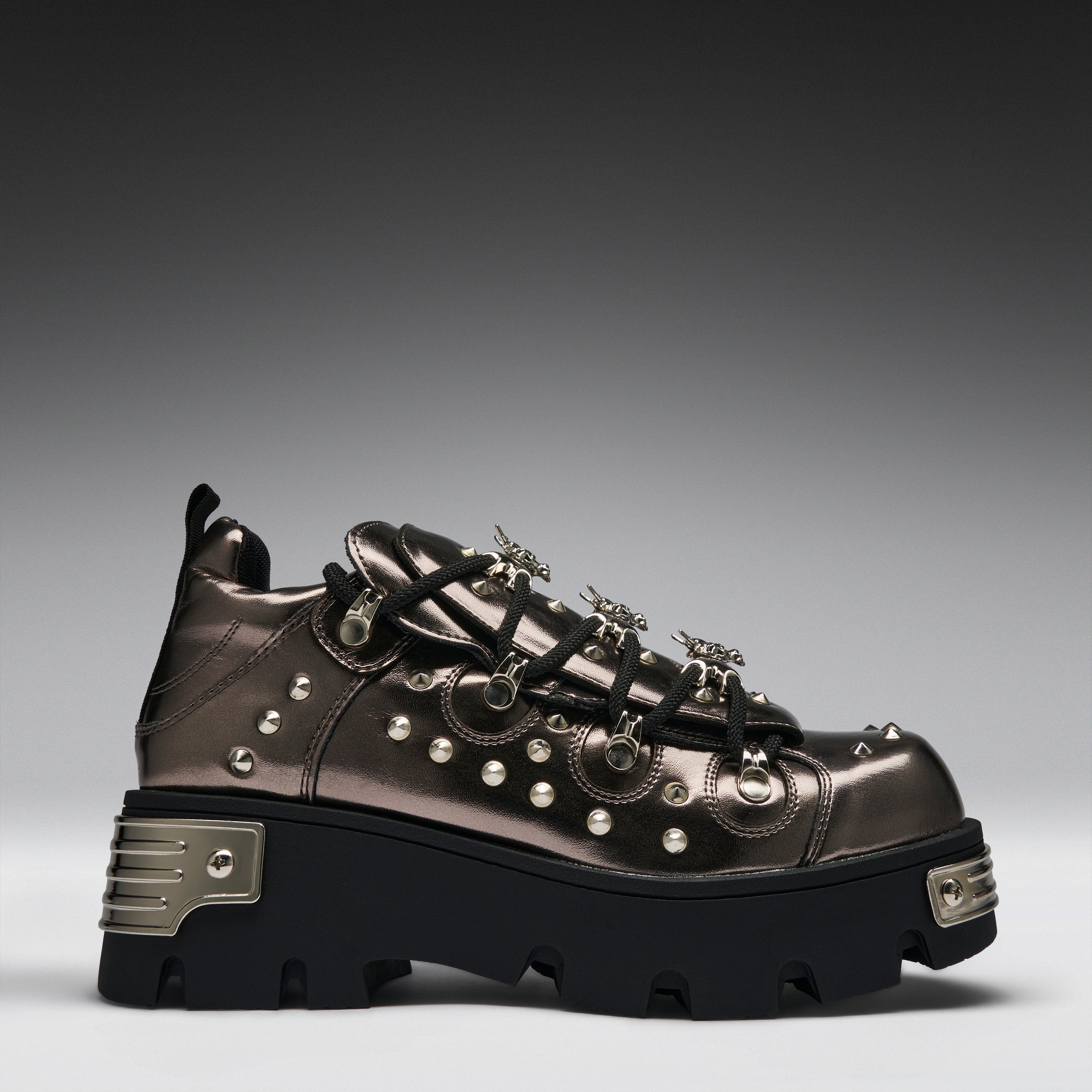 A metallic bronze high-top sneaker with black laces, silver studs, and a chunky black platform sole with silver metal accents, shown against a dark gray gradient background.
