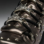 Close-up of a metallic dark brown leather sneaker with black laces, silver studs, and ornate silver metal eyelets.
