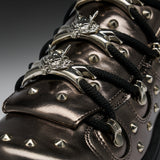 Close-up of a metallic dark brown leather sneaker with black laces, silver studs, and ornate silver metal eyelets.