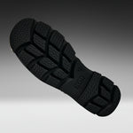 A close-up of a black rubber shoe sole with deep tread patterns, shown diagonally against a dark-to-light gray gradient background.