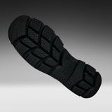A close-up of a black rubber shoe sole with deep tread patterns, shown diagonally against a dark-to-light gray gradient background.