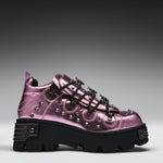 A metallic pink platform sneaker with black laces, silver studs, and a chunky black sole, shown from a side profile on a gray gradient background.