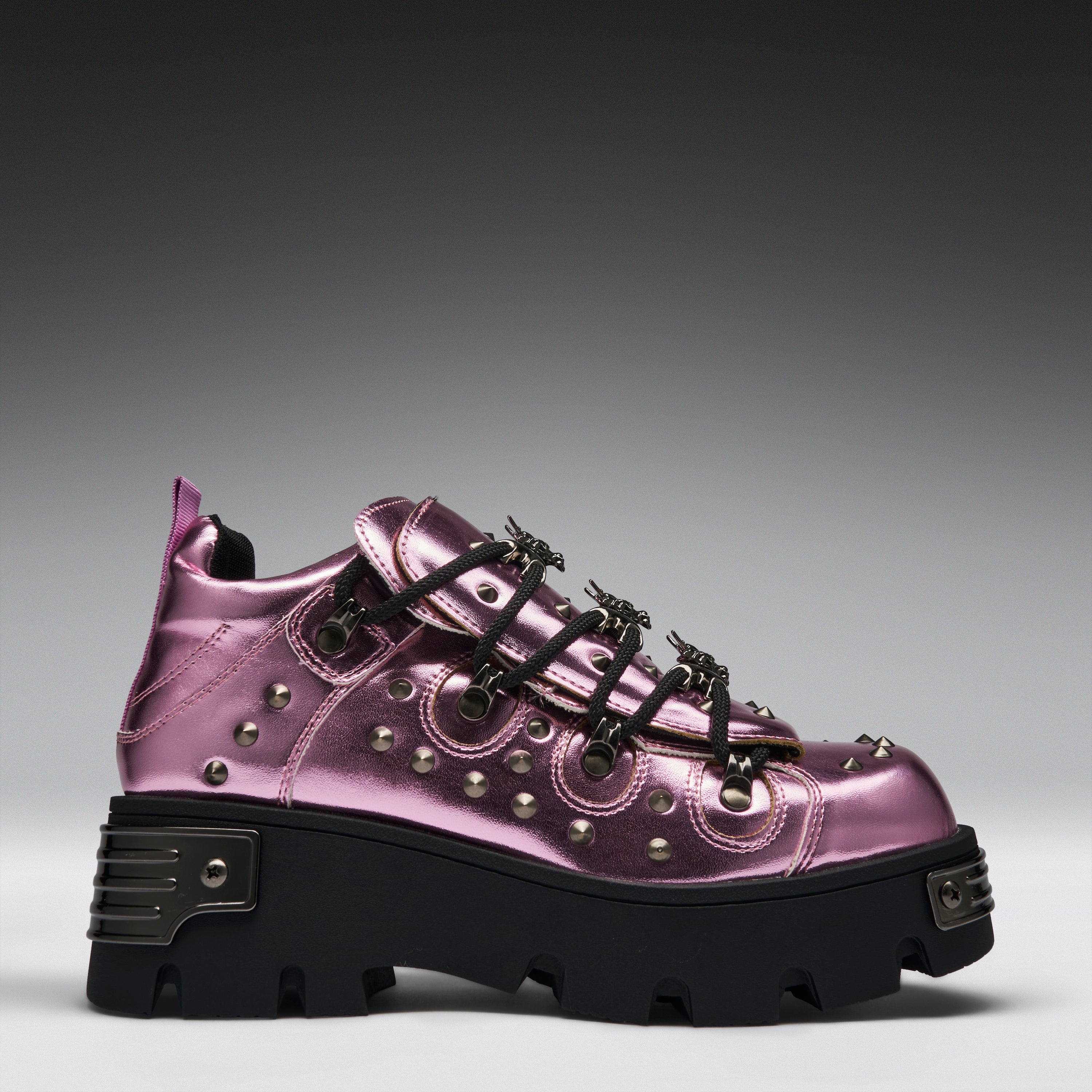 A metallic pink platform sneaker with black laces, silver studs, and a chunky black sole, shown from a side profile on a gray gradient background.