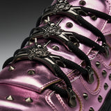 Close-up of a metallic pink high-top sneaker with black laces, silver conical studs, and ornate silver lace hardware featuring a wolf head design.