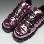 Metallic pink high-top sneakers with black laces, decorative metal eyelets, and chunky black soles, photographed on a clean gray studio background.