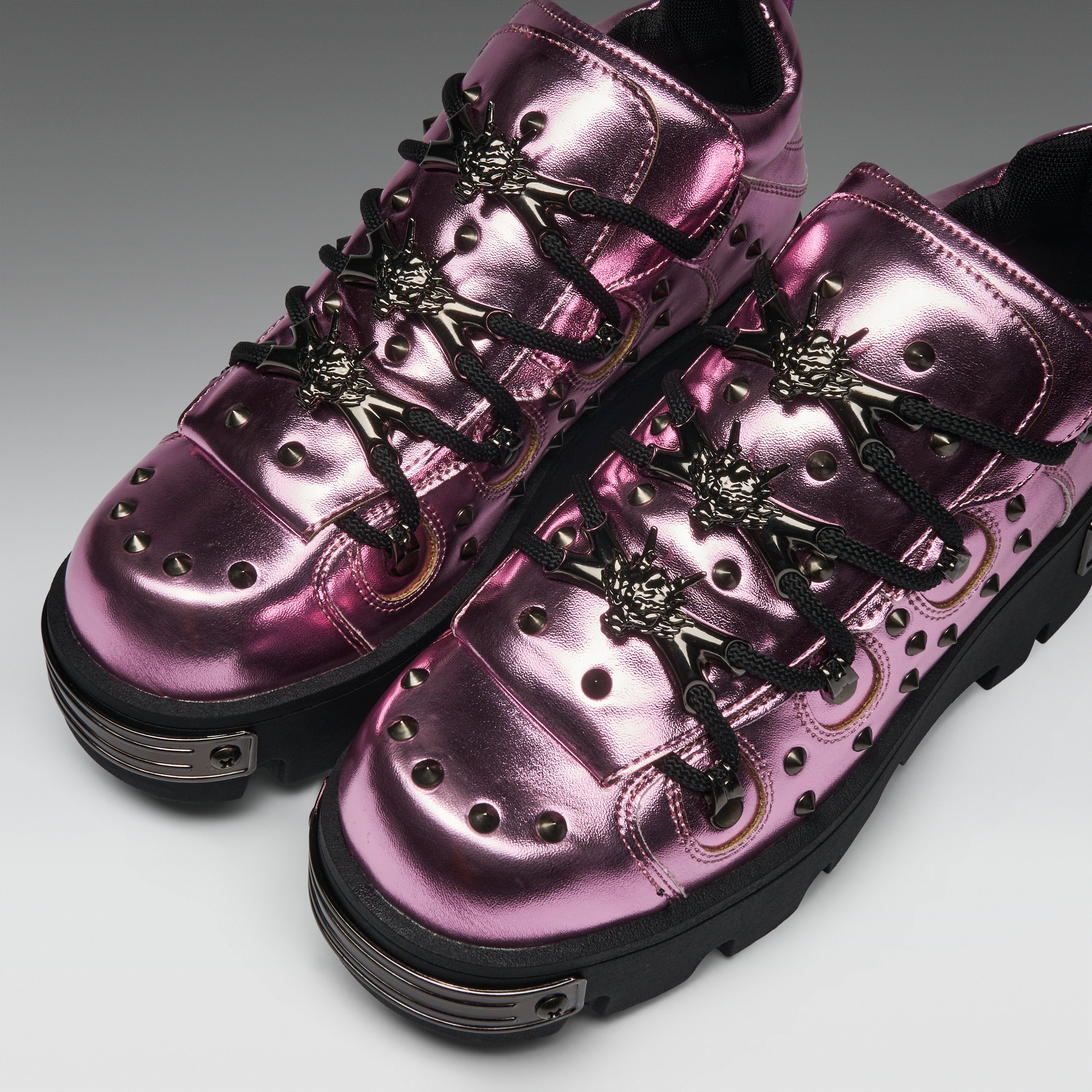 Metallic pink high-top sneakers with black laces, decorative metal eyelets, and chunky black soles, photographed on a clean gray studio background.