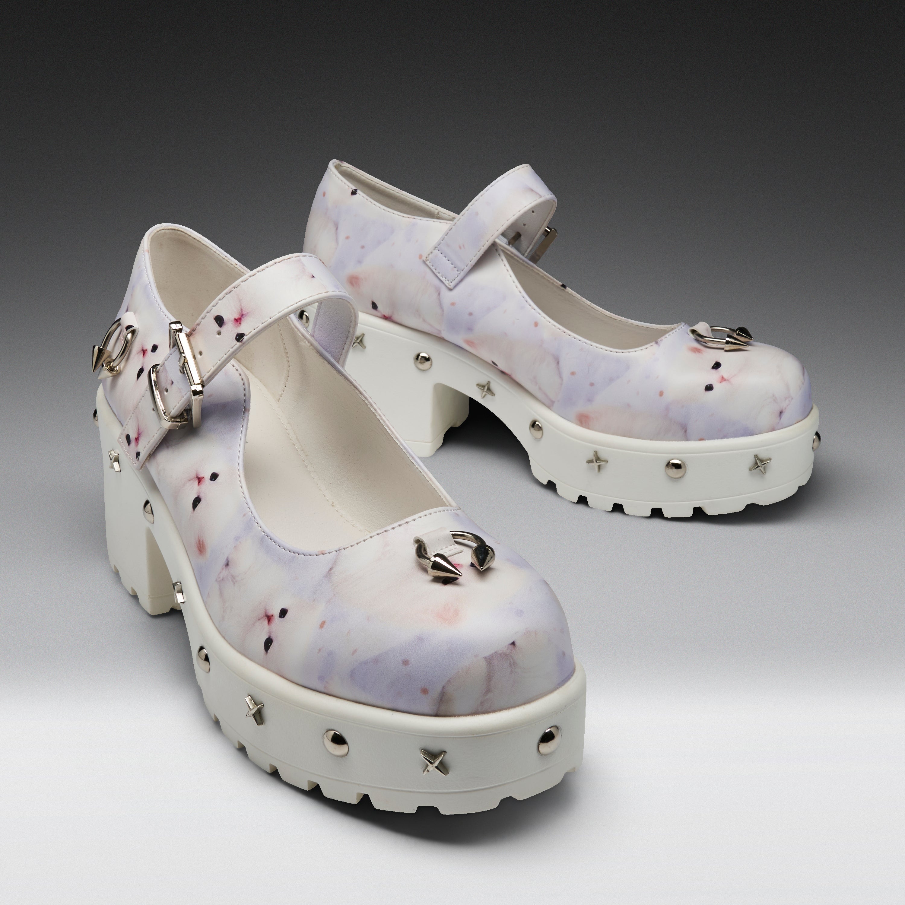 A pair of Mary Jane platform heels with a white and light purple watercolor pattern, decorated with silver buckles, spikes, and a metallic bow on the toe, set against a dark gray gradient background.