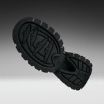 A close-up of a black rubber shoe sole with textured tread patterns and embossed branding, shown against a dark-to-light gray gradient background.