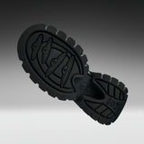 A close-up of a black rubber shoe sole with textured tread patterns and embossed branding, shown against a dark-to-light gray gradient background.