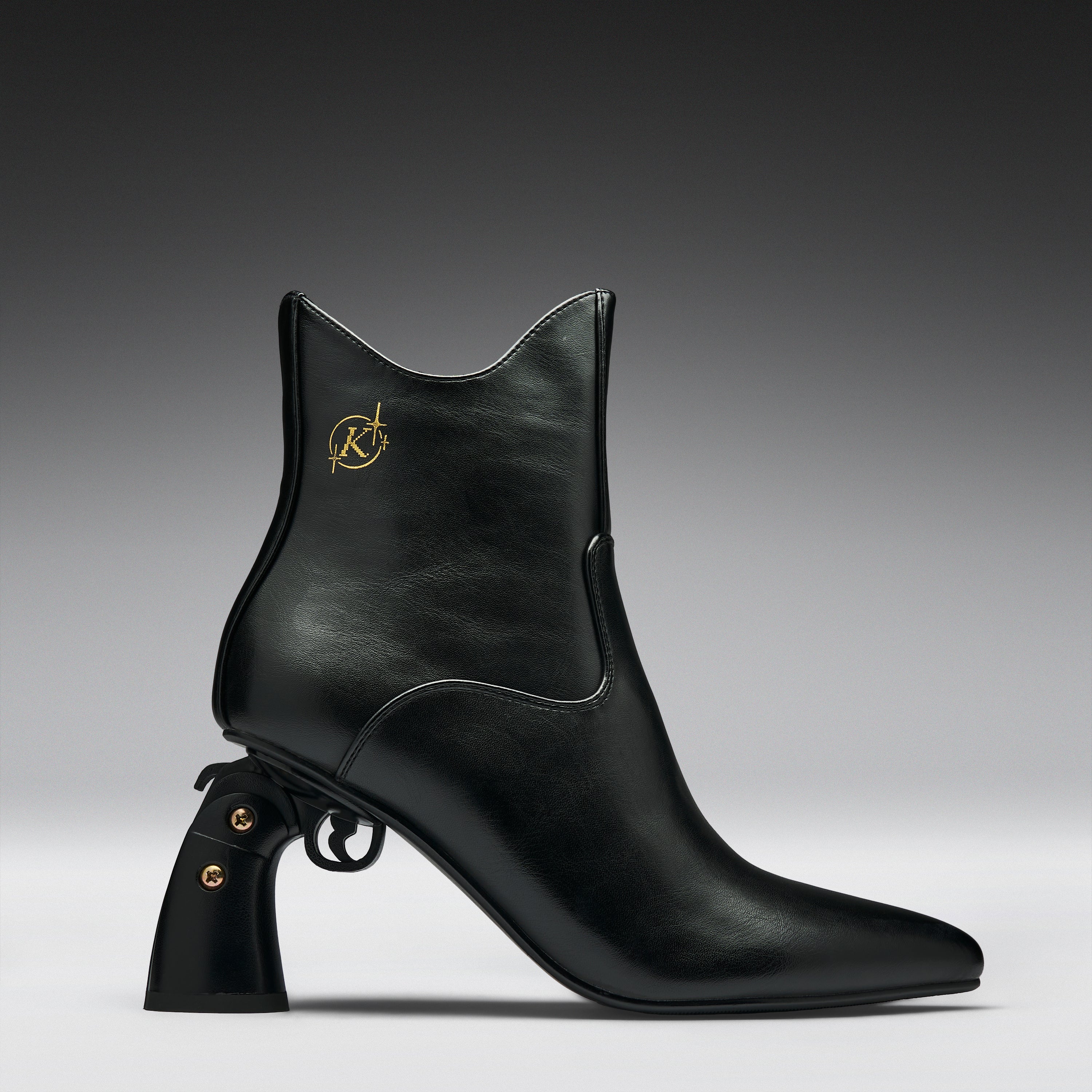 A black leather ankle boot with a pointed toe, a unique pistol-shaped block heel, and a gold Karl Lagerfeld logo on the side, shown against a dark gray gradient background.