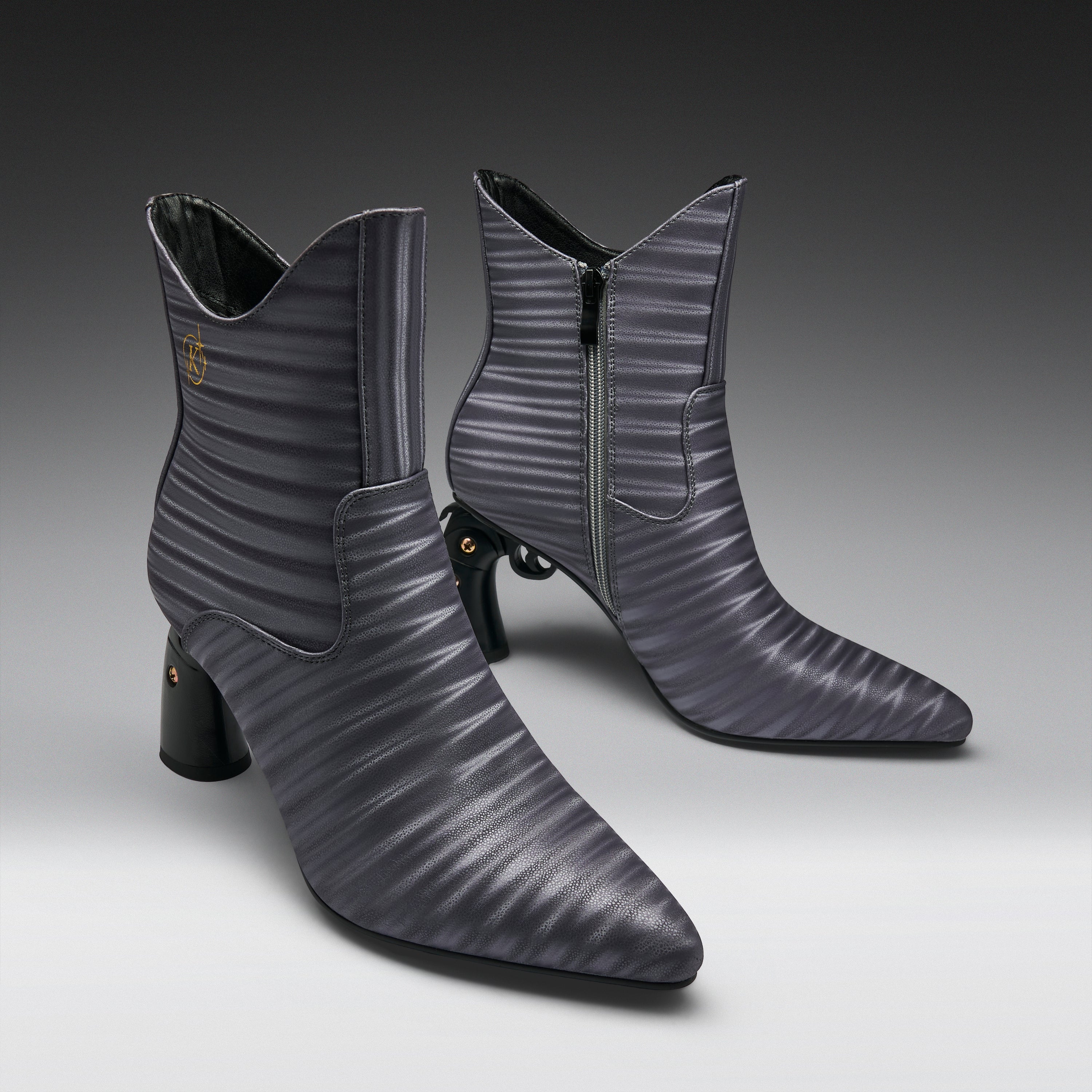 A pair of pointed-toe ankle boots in a dark gray ribbed leather, featuring a mid-height block heel, side zipper, and a small gold logo on the inner side, set against a dark-to-light gray gradient studio background.