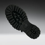 A close-up of a black rubber shoe sole, showing the deep lugs and tread pattern, photographed against a dark-to-light gray gradient background.
